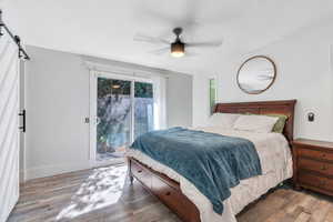 Bedroom featuring a barn door, access to outside, light wood-style floors, and a ceiling fan