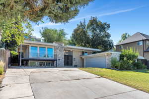 Mid-century inspired home featuring a balcony, stone siding, driveway, brick siding, and an attached garage