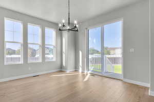 Unfurnished dining area featuring a chandelier, light wood-type flooring, and healthy amount of natural light