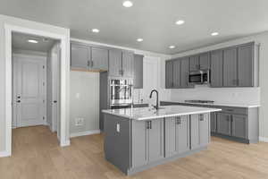 Kitchen with gray cabinetry, recessed lighting, light wood finished floors, decorative backsplash, and a center island with sink