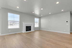 Unfurnished living room with recessed lighting, a glass covered fireplace, light wood finished floors, and a textured ceiling