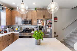 Kitchen with appliances with stainless steel finishes, brown cabinetry, a textured ceiling, hanging light fixtures, and wood finished floors