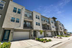 Modern home with driveway, a balcony, an attached garage, a residential view, and stucco siding
