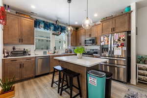 Kitchen featuring stainless steel appliances, decorative light fixtures, a kitchen island, a kitchen breakfast bar, and a textured ceiling