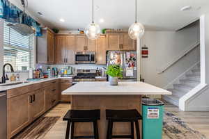 Kitchen with appliances with stainless steel finishes, brown cabinetry, a center island, a breakfast bar area, and light wood-style flooring