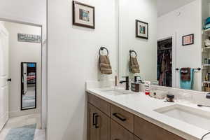 Ensuite bathroom featuring double vanity, a walk in closet, and light tile patterned floors