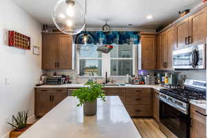 Kitchen featuring appliances with stainless steel finishes, a textured ceiling, brown cabinets, light wood-style floors, and decorative light fixtures