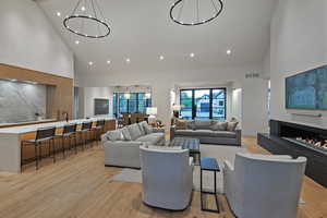Living room featuring high vaulted ceiling, light wood-type flooring, recessed lighting, and a warm lit fireplace
