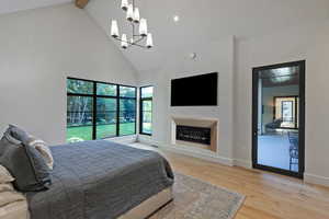Bedroom with a glass covered fireplace, light wood-type flooring, high vaulted ceiling, and beamed ceiling