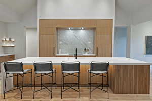 Kitchen with a breakfast bar area, modern cabinets, a center island with sink, open shelves, and high vaulted ceiling