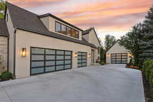 Property exterior at dusk with concrete driveway, stucco siding, a garage, and a shingled roof