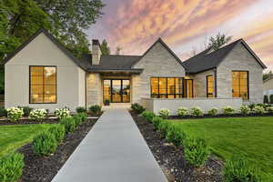 View of front of home with stone siding, a lawn, a chimney, and a shingled roof