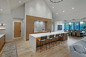 Kitchen with high vaulted ceiling, modern cabinets, a large island with sink, recessed lighting, and light wood finished floors