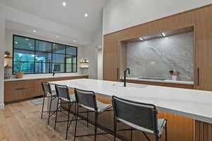 Kitchen featuring modern cabinets, open shelves, a breakfast bar area, light wood-type flooring, and high vaulted ceiling