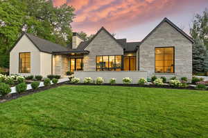View of front facade featuring a chimney, a lawn, and stone siding