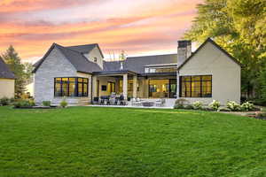 Back of house at dusk featuring stone siding, a patio area, a chimney, a yard, and outdoor lounge area