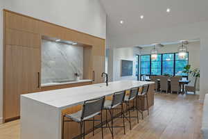 Kitchen with a breakfast bar area, modern cabinets, light wood finished floors, high vaulted ceiling, and a center island with sink