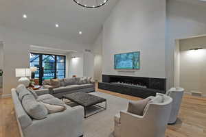 Living area with light wood-style flooring, high vaulted ceiling, a high end fireplace, and recessed lighting