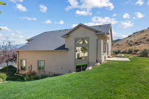 Back of property with a lawn, stucco siding, a shingled roof, and a patio area
