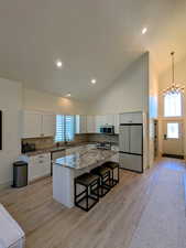 Kitchen featuring a breakfast bar, stainless steel appliances, a kitchen island, tasteful backsplash, and high vaulted ceiling