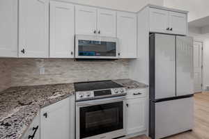 Kitchen with appliances with stainless steel finishes, white cabinetry, light stone counters, backsplash, and light wood-style floors