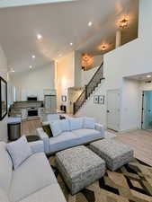 Living room with light wood-style floors, high vaulted ceiling, recessed lighting, and stairs