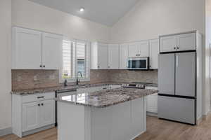 Kitchen with appliances with stainless steel finishes, light stone counters, white cabinets, light wood-type flooring, and high vaulted ceiling