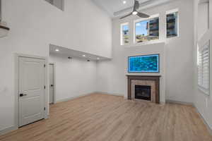 Unfurnished living room featuring a ceiling fan, light wood-style flooring, a fireplace, a towering ceiling, and recessed lighting