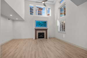 Unfurnished living room featuring a high ceiling, light wood-style floors, a ceiling fan, and a fireplace