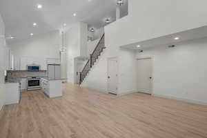 Unfurnished living room with high vaulted ceiling, recessed lighting, light wood-style floors, a chandelier, and stairs