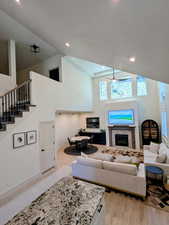 Living room featuring high vaulted ceiling, light wood-style floors, recessed lighting, a fireplace, and stairs