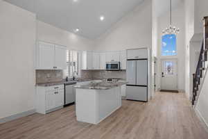 Kitchen with appliances with stainless steel finishes, high vaulted ceiling, a center island, light stone counters, and backsplash