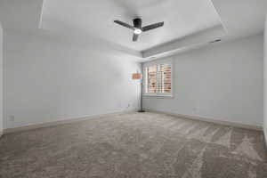 Spare room featuring a raised ceiling, light colored carpet, a ceiling fan, and a textured ceiling