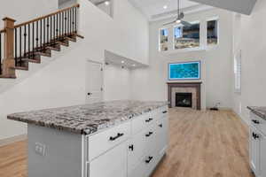Kitchen featuring a fireplace, light wood-style floors, a center island, light stone counters, and white cabinetry