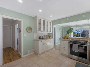 Kitchen featuring electric stove, glass insert cabinets, white cabinets, light stone counters, and backsplash