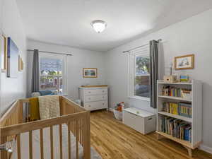 Bedroom with light wood-type flooring, multiple windows, and a nursery area
