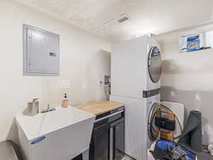 Laundry room with electric panel, stacked washing machine and dryer, and a textured ceiling