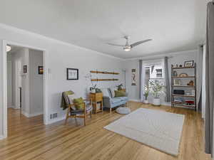 Sitting room with ornamental molding, a ceiling fan, light wood-style floors, and a textured ceiling