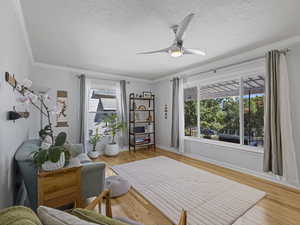 Sitting room featuring ornamental molding, light wood-style flooring, a ceiling fan, and a textured ceiling
