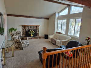 Living area featuring beamed ceiling, a stone fireplace, carpet, and high vaulted ceiling