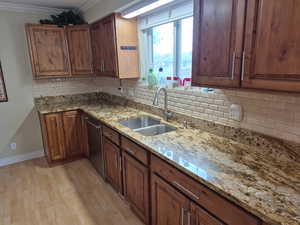 Kitchen with decorative backsplash, crown molding, light stone counters, light wood finished floors, and dishwasher