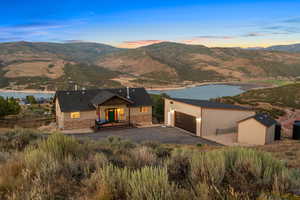 View of front facade featuring an outbuilding, a patio area, a mountain view, stone siding, and driveway