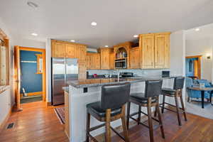 Kitchen with stainless steel appliances, light brown cabinetry, a kitchen breakfast bar, recessed lighting, and dark wood-style flooring