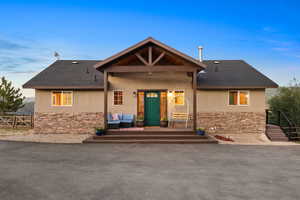 View of front facade featuring stone siding, stucco siding, a patio, and roof with shingles