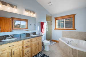 Bathroom with a jetted tub, a stall shower, double vanity, light tile patterned floors, and vaulted ceiling
