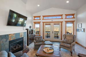Living area with carpet, plenty of natural light, french doors, high vaulted ceiling, and a fireplace