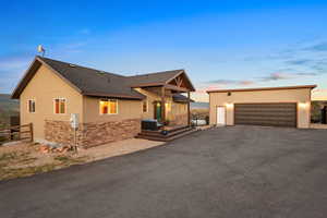 View of front of house with roof with shingles, stone siding, an outbuilding, a patio area, and a garage