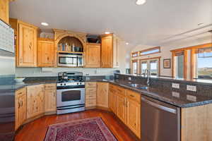 Kitchen featuring stainless steel appliances, dark wood-style floors, open shelves, dark stone counters, and recessed lighting