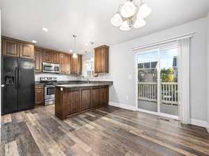 Kitchen with stainless steel appliances, hanging light fixtures, recessed lighting, dark stone countertops, and a peninsula