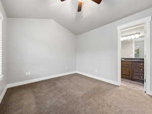 Unfurnished bedroom featuring light colored carpet, lofted ceiling, ceiling fan, and ensuite bathroom